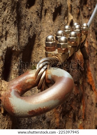 Eye bolt with iron rope anchored into sandstone rock. Twisted rope of climber safety path fixed in block by screws snap hooks.