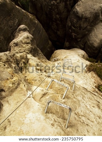 Iron cramps in rock, tourist ladder. Iron twisted rope fixed in block by screws snap hooks. The rope end anchored into sandstone rock. Climbers way.
