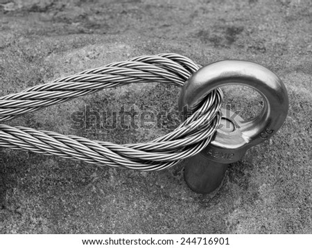 Climbers equipment. Iron twisted rope fixed in block by screws snap hooks. The rope end anchored into sandstone rock. Black and white photo.