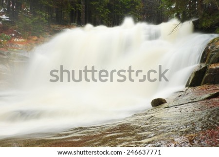 Huge stream of water is falling into foamy pond below. High cascade in forest. Crystal freeze water of mountain river.