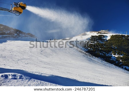 Snow making on slope. Skier near a snow cannon making fresh powder snow. Mountain ski resort and winter calm mountain landscape.