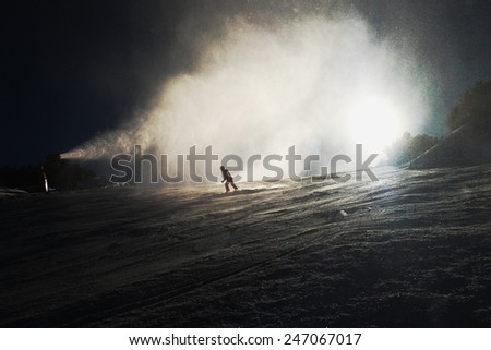 Snow making on slope. Skier near a snow cannon making fresh powder snow. Mountain ski resort and winter calm mountain landscape.