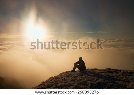 Tired hiker in black sit on frozen grass on hill and watching into misty daybreak. Autumn misty day in mountains.
