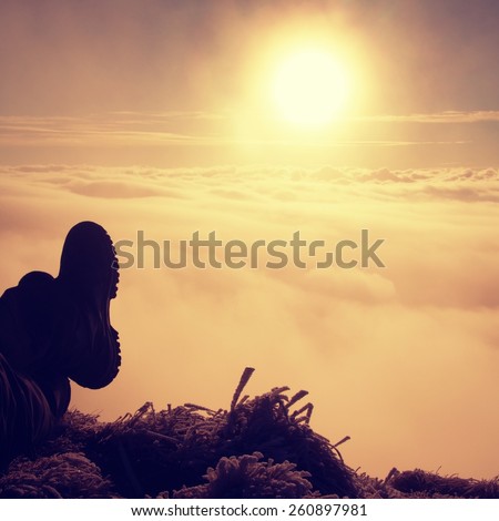 Man legs in big boots laying on the ground in a frozen grass, resting on a hill. Tired hiker and  watching into misty daybreak. Autumn misty day in mountains.