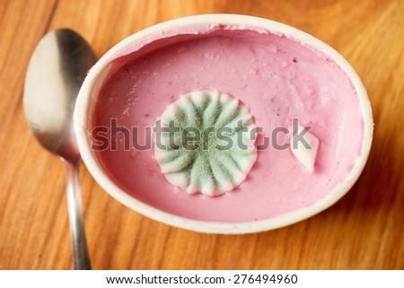 Plastic cup of pink fruit yogurt with ugly circle blossom of poisonous mold. Stainless spoon.