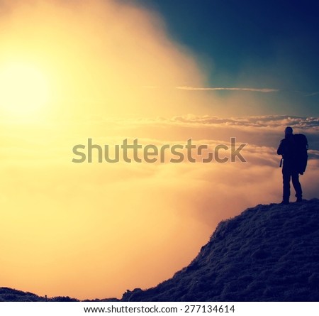 Happy hiker in black on the peak of the world. Heavy orange mist bellow in valley. Wonderful daybreak in mountains.