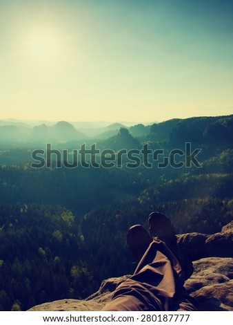Long tired male legs in hiking trousers take a rest on peak of rock above valley.