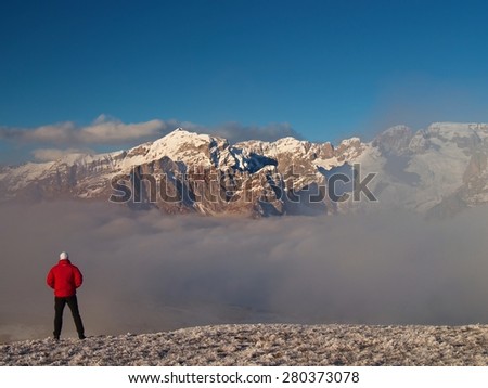 Tourist in red winter jacket on snowy view point. National park Alps park in Italy. Sunny winter morning.