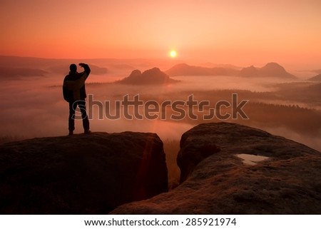 Happy hiker on top of the world. Man is standing on the peak of  rock empires park and watching over the misty and foggy morning valley to Sun.