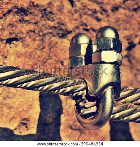 Detail of chrome screws snap hooks and grommets at and of rope. Iron twisted rope fixed together by screws snap hooks. Detail of rope end anchored at sandstone rock
