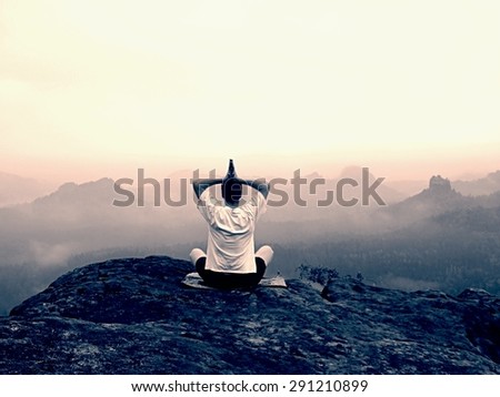 Alone man is doing Yoga pose on the rocks peak within misty morning
