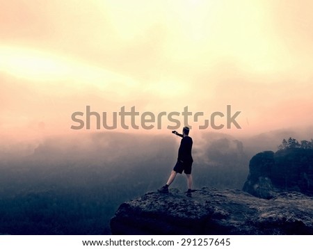 Tall tourist in pants is taking photo on the rocky peak at sunrise. Mist in rocky mountains