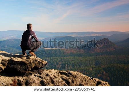 Climbing adult man at the top of  rock with aerial view of the deep misty valley bellow