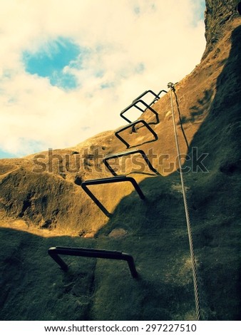 Climbers way. Iron ladder and iron twisted rope fixed in block by screws snap hooks. The rope end anchored into sandstone rock.