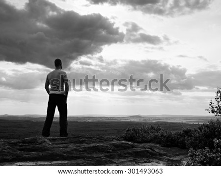 Adult sportsman on the cliff in rocky mountains park and watch into landscape. Black and white photo