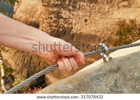 Rock climber\'s hand hold on steel twisted rope at steel bolt eye anchored in sandstone rock. Tourist path via ferrata.