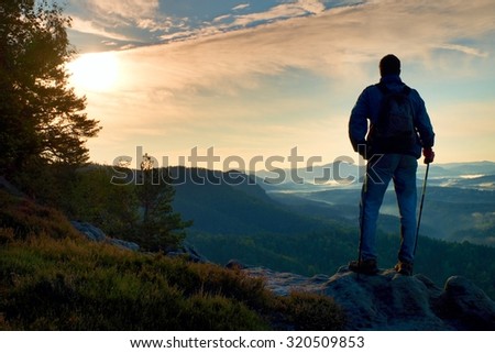 Silhouette of tourist. Sunny spring daybreak in rocky mountains. Hiker with sporty backpack stand on rocky view point above misty valley.