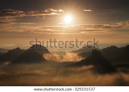 Autumn sunset view over forest to fall colorful valley full of dense mist colored with hot  sun rays
