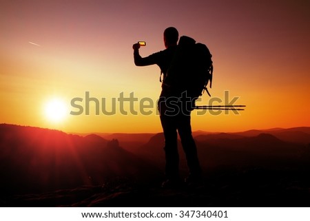 Strong man hiker taking photo with smart phone at mountain peak. Marvelous daybreak at horizon.
