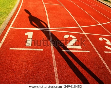 Athlete dark sharp body shadow on a red running track in stadium