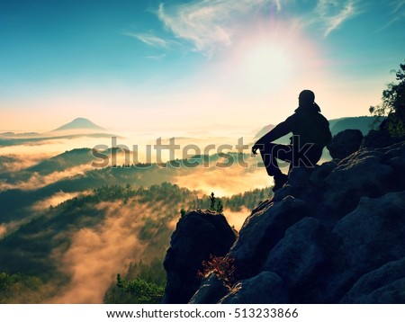 Hiker man take a rest on mountain peak. Man lay on summit, bellow autumn valley. Bright morning Sun shining in sky.