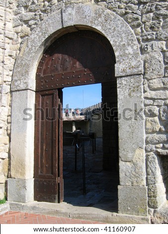 Old open arched wooden door set into an old gray stone wall