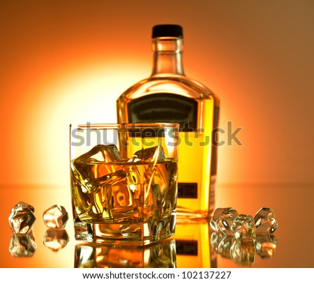 Glass of whiskey on the rocks with a bottle in the background