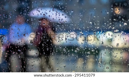 Pedestrians crossing the street in the rain, view through a rainy window