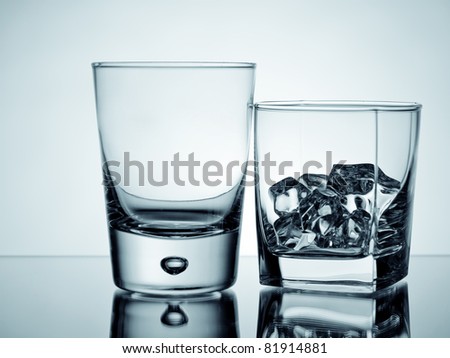 An empty glass and a tumbler with ice cubes