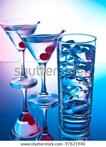 Two glasses of martini with red cherries and a glass of clear cocktail