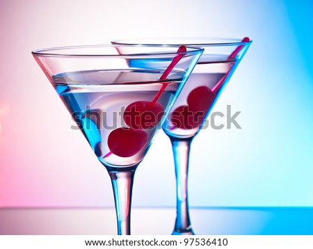 Two glasses of martini with red cherries on a mixed color background