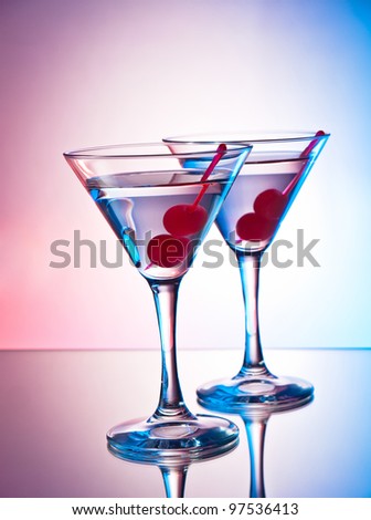Two glasses of martini with red cherries on a mixed color background