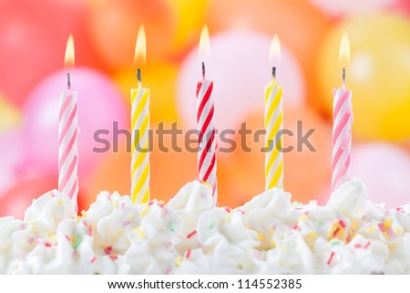 Five lit birthday candles on colorful balloons background