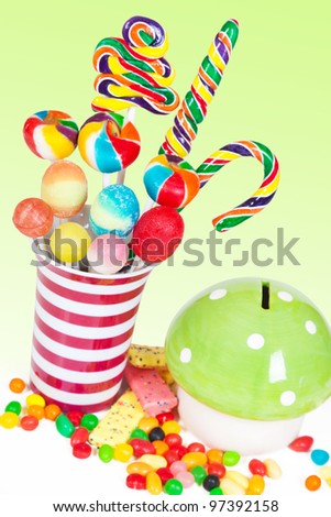 Colorful lollipops in a jar and more candies and a piggy bank in a table. Kids birthday table setting