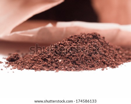 Pile of ground coffee on a white table with a bag