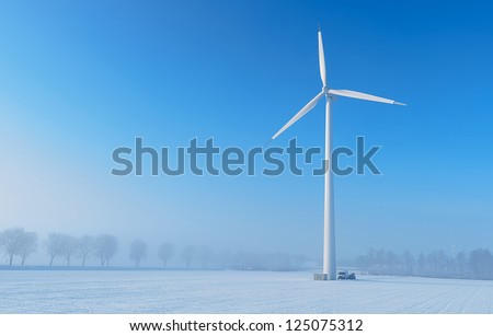 Maintenance on a giant wind turbine in a cold and foggy winter landscape