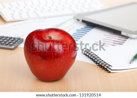 Ripe red apple on workplace with financial papers and computers