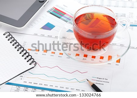 Tea cup on contemporary workplace with financial papers, office supplies and tablet