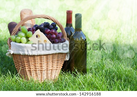 Outdoor picnic basket with bread, cheese and grape and wine bottles on lawn