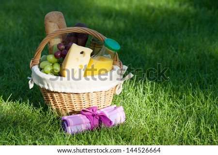 Outdoor picnic basket with bread, cheese and grape on green lawn