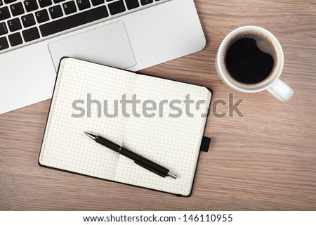 Notepad, laptop and coffee cup on wood table. View from above