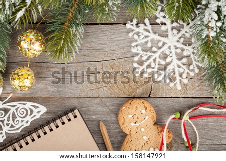 Christmas fir tree covered with snow, decor and blank notepad on wooden board background