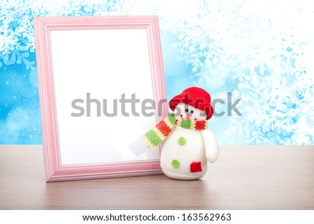 Blank photo frame and christmas snowman on wooden table over blue christmas background