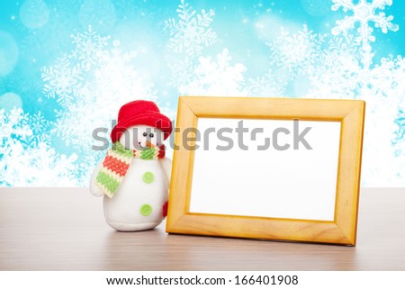 Blank photo frame and christmas snowman on wooden table over blue christmas background