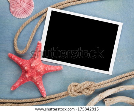 Blank photo frame with seashells, ship rope, sea stones over blue wooden background