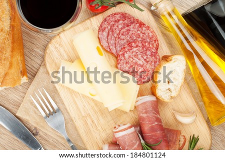 Red wine with cheese, prosciutto, bread, vegetables and spices on wooden table