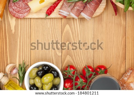 Red wine with cheese, olives, tomatoes, prosciutto, bread and spices. Over wooden table background. View from above with copy space
