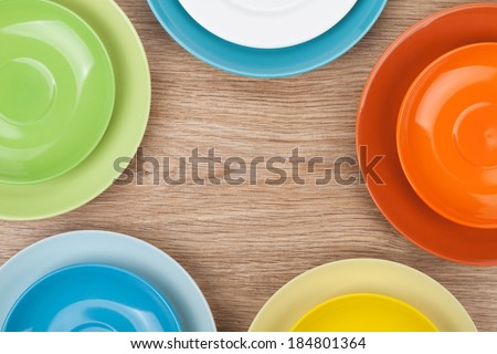 Colorful plates and saucers over wooden table background. View from above with copy space