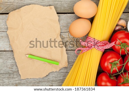 Pasta, tomatoes, eggs and blank brown paper for copy space on wooden table background