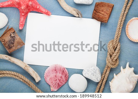 Blank paper card with seashells, ship rope, sea stones over blue wooden background